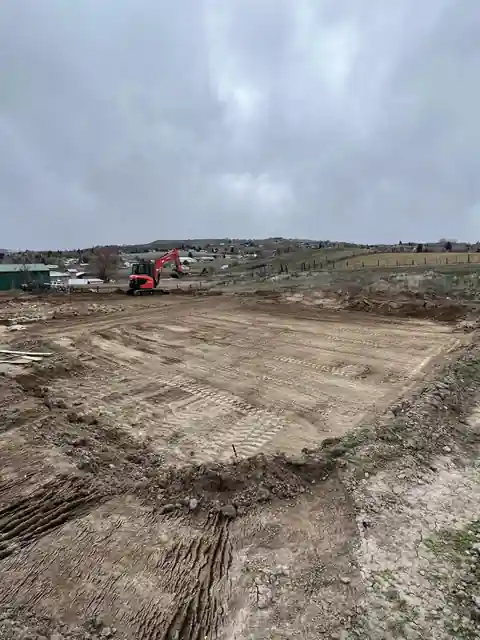 A freshly dug building pad next to an orchard, excavator in the distance