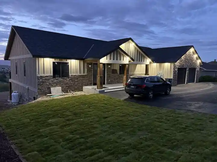 Finished board-and-batten home with stacked-stone wainscot and soffit lights on at dusk