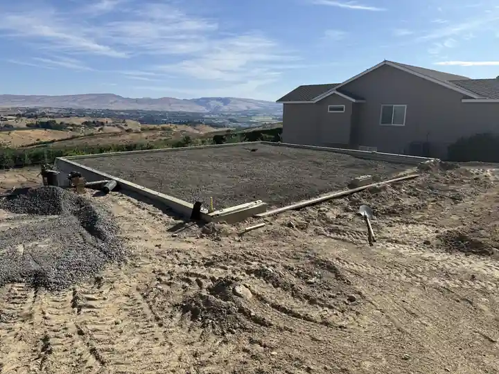 Foundation stem walls and a gravel pad beside a finished home in the valley