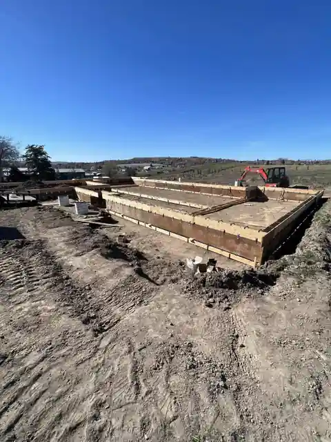 Foundation wall forms standing on a job site with an excavator behind
