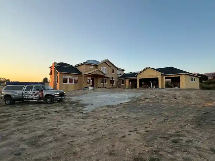 Silver LF Construction & Excavating pickup parked in front of a sheathed two-storey custom home and three-bay garage at sunset