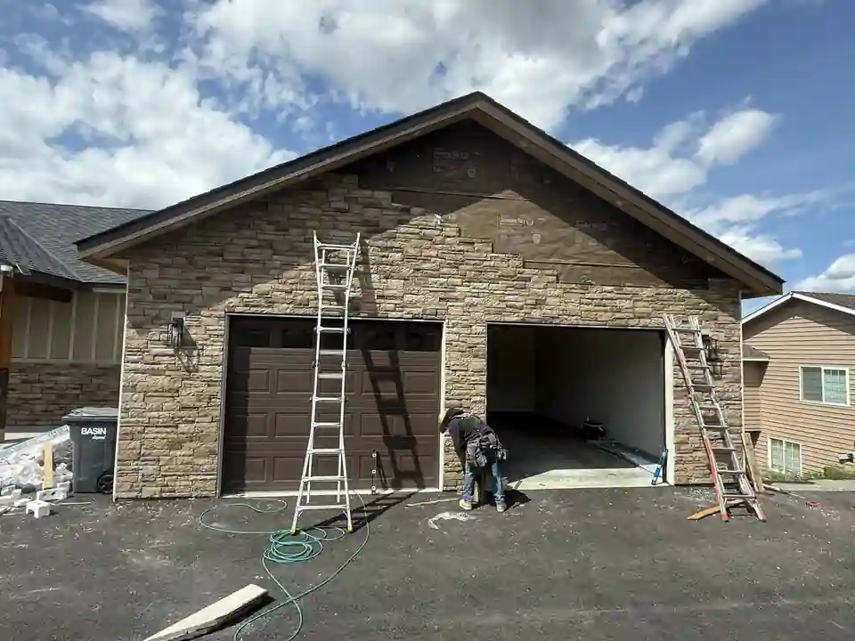 Stone-front garage gable with siding above and a worker at the door