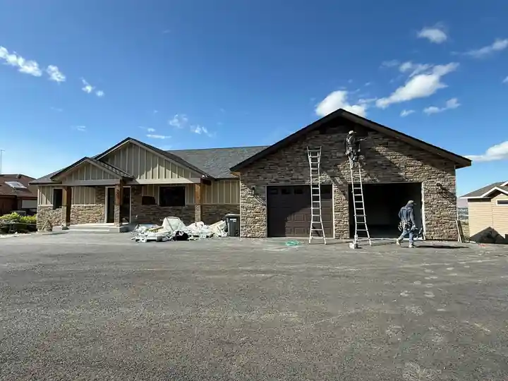 The stacked-stone house during siding, LF crew on ladders at the garage gable