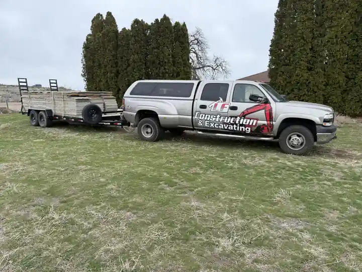 Silver LF Construction pickup hitched to a flatbed equipment trailer on a grass lot