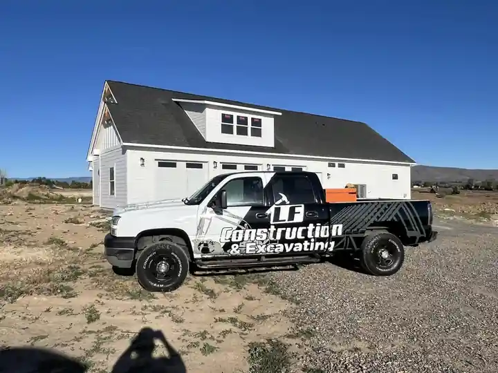 White LF Construction pickup in front of a new white farmhouse-style home with a three-car garage